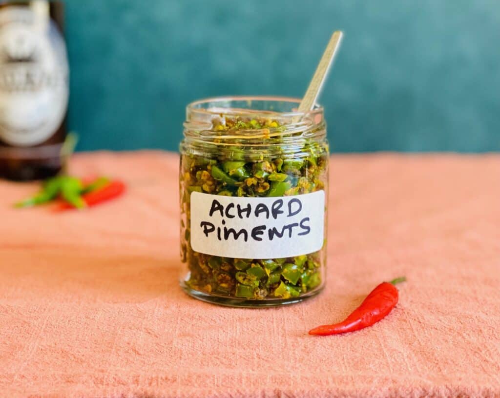 Mauritian Green Chili Achard in a glass jar and a stainless steel spoon inside the jar.