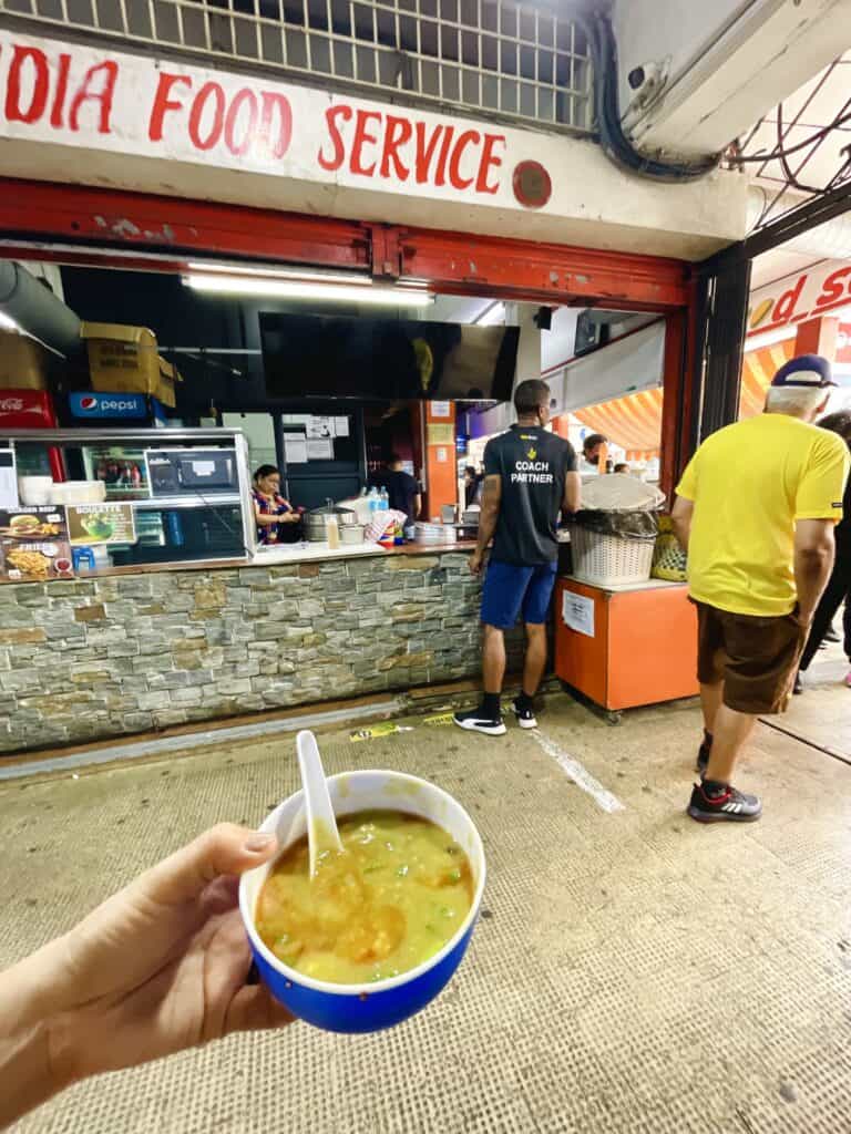 Front of Halim vendor in Rose Hill - Little India Food Service. Bowl of halim with hand holding it.