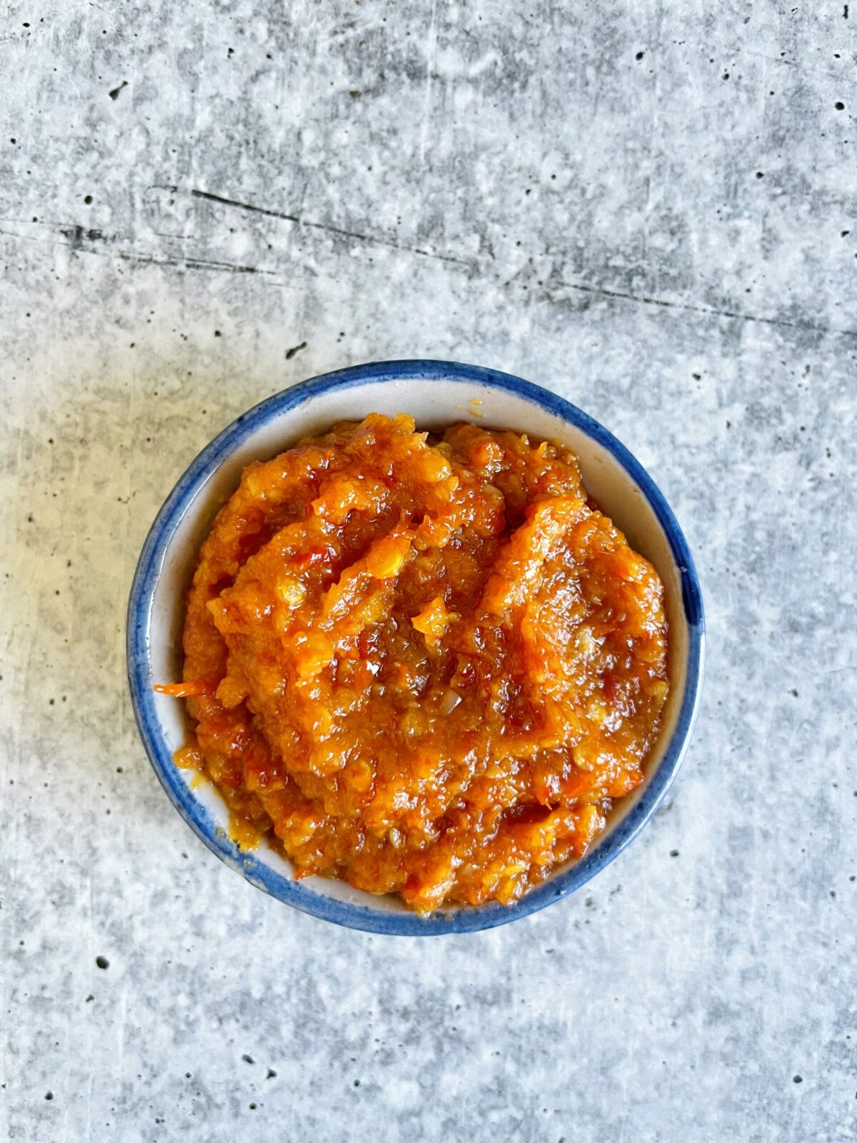 Mauritian Homestyle Chinese red chili paste in a small blue and white porcelain bowl on a cement surface.