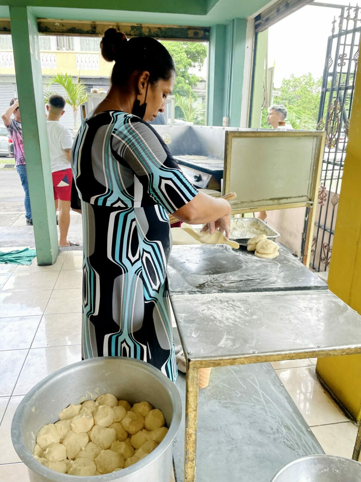Mauritian roti dough balls in aluminum deksi - SKB Roti vendor with lady rolling fresh roti on table.