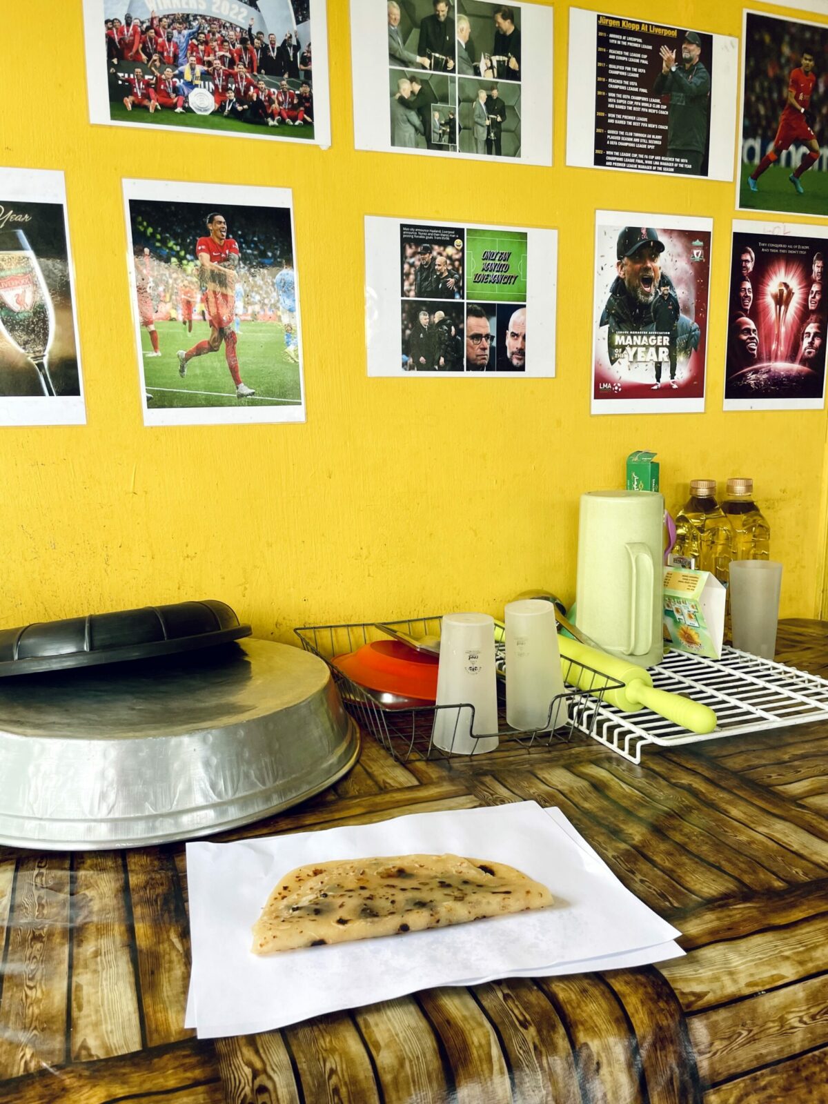 Folded Mauritian roti on white paper and table with soccer posters on wall and utensils drying on rack - SKB Roti vendor Port Louis.