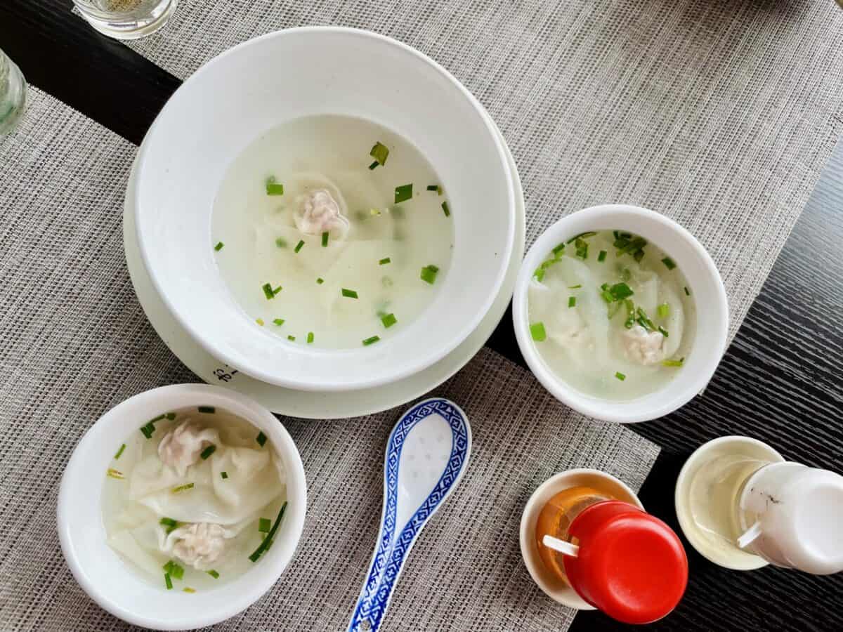 Wantan soup in large bowl and two small serving bowls and Chinese blue porcelain spoon. Chinese red chili paste and mustard on the side - Noodle Square Restaurant.