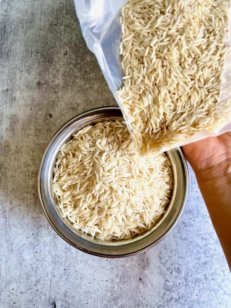 Aged basmati rice being poured into a stainless steel bowl.