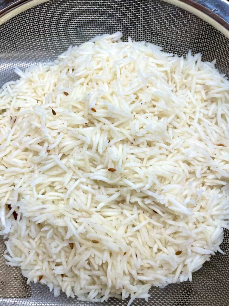 Partially cooked basmati rice, and cumin seeds in strainer