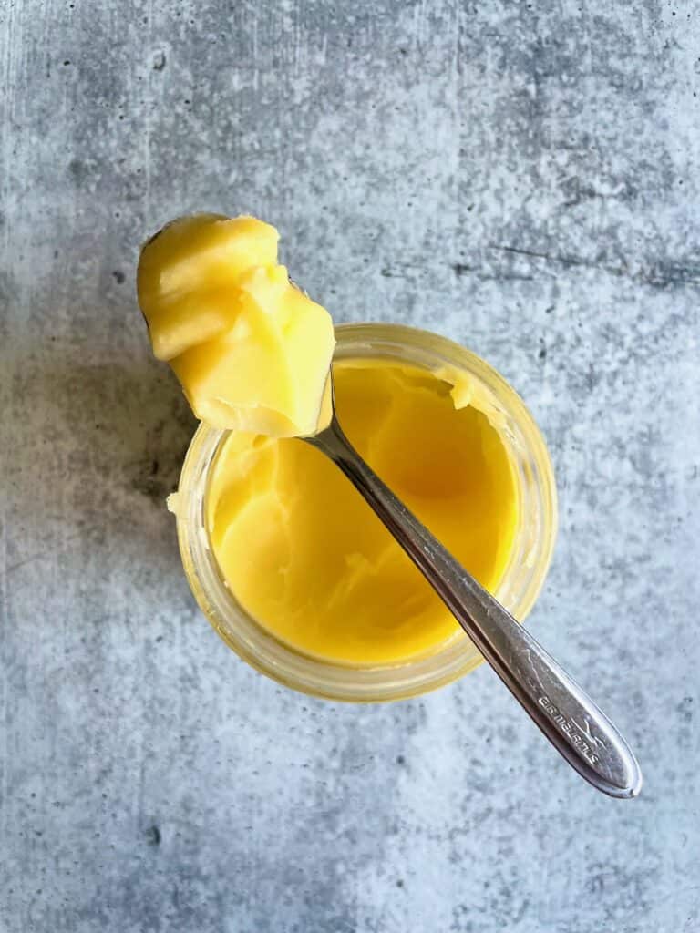 Cultured ghee on a teaspoon balancing over a ghee jar