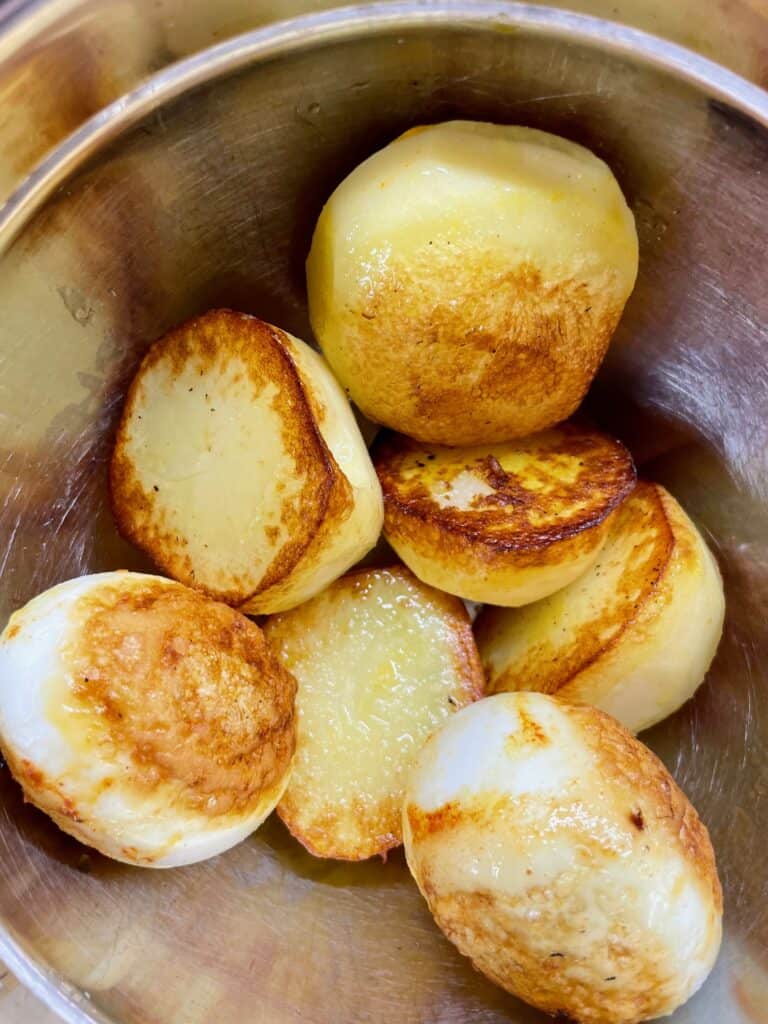 Fried hard boiled eggs and half cooked potatoes in stainless steel bowl