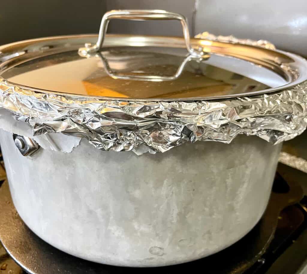 Heavy bottom stockpot with aluminum foil and lid on, and on top of a cast iron tawa.