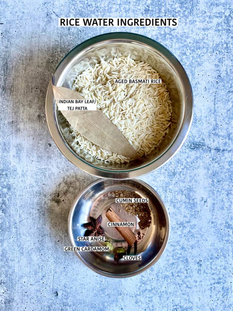 Ingredients for parboiling basmati rice for briani: aged basmati rice and Indian bay leaf in one medium stainless steel bowl and another small stainless steel bowl of cumin seeds, cinnamon stick, whole star anise, green cardamom pods and cloves.