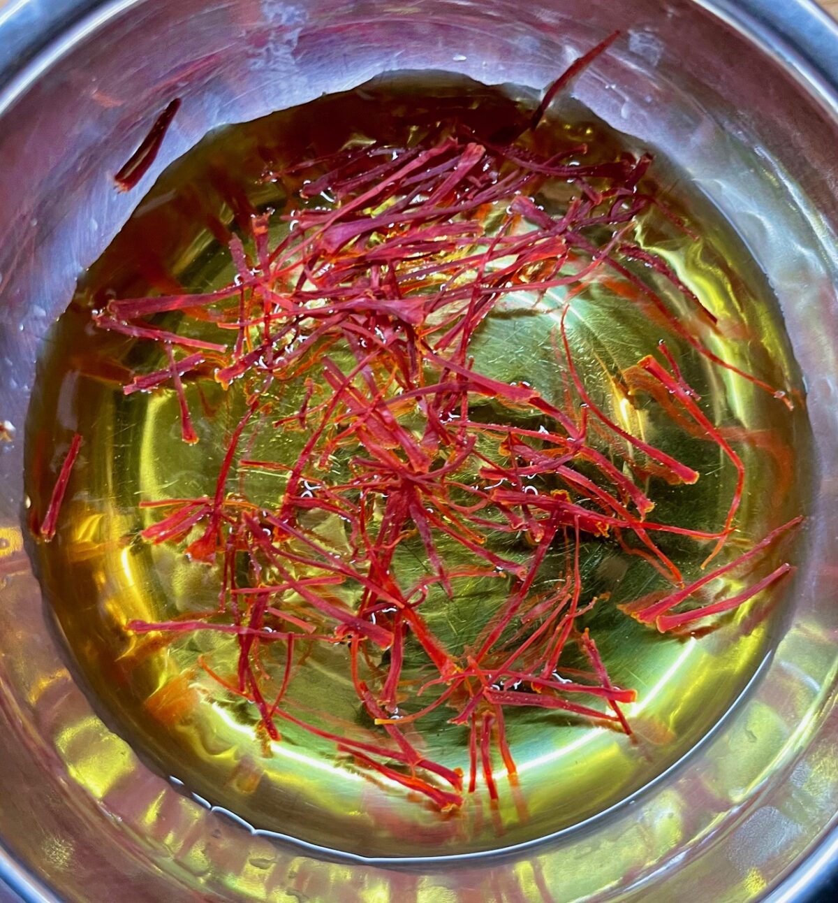 Saffron mixed with water in a bowl in a stainless steel bowl.