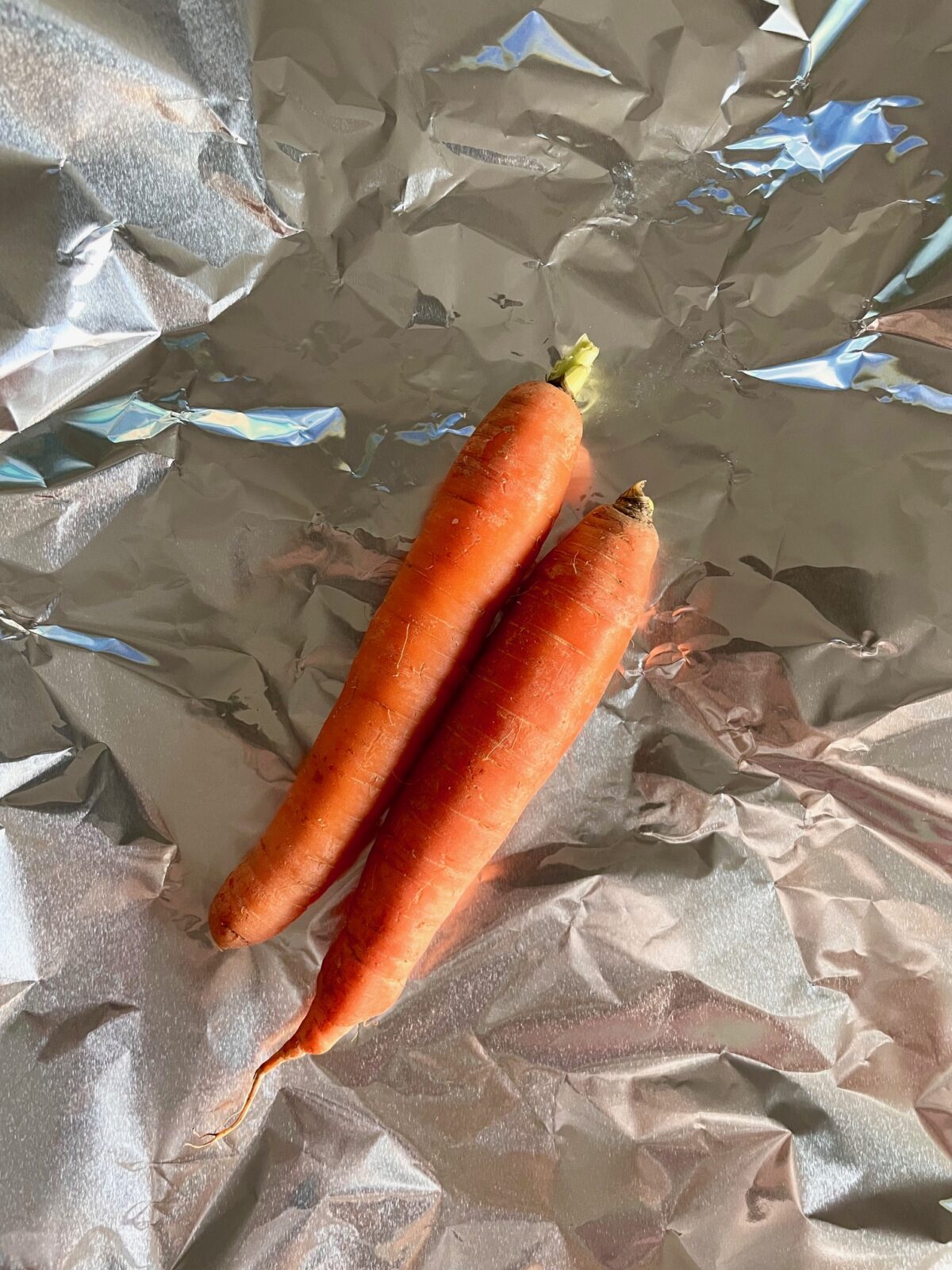 Two orange carrots on aluminum foil.