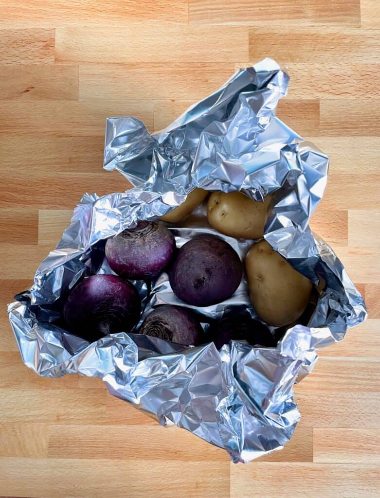 Potatoes and Beets partly wrapped in foil on wooden surface.