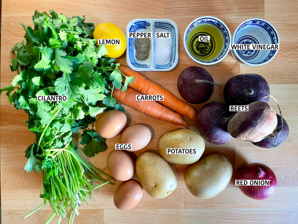 Ingredients for beet and potato salad, namely: fresh cilantro bunch, eggs, yellow potatoes, beets, red onion, orange carrots, white vinegar, lemon, vegetable oi, salt and pepper.
