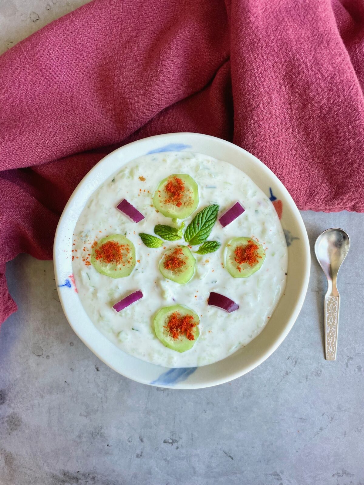 Cucumber raita for biryani in a bowl, and a small spoon next to it.