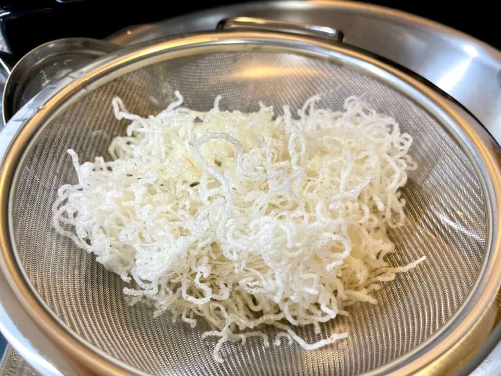 Fried rice vermicelli in strainer over large stainless steel bowl.