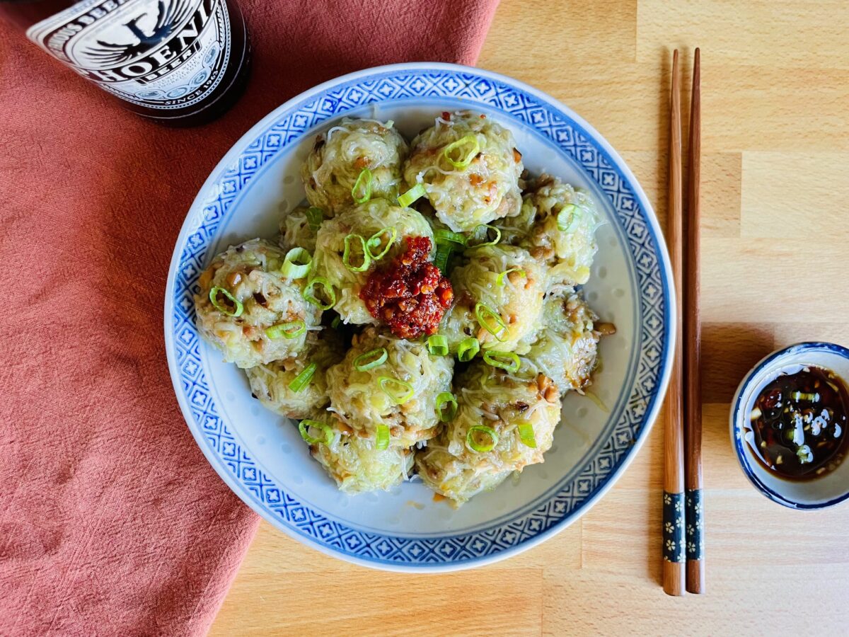 Niouk yen with red chili paste and topped with chopped green onion in Chinese blue and white rice plate. Wooden chopsticks and soy sauce next to it the plate. Mauritian Phoenix beer bottle in the background.