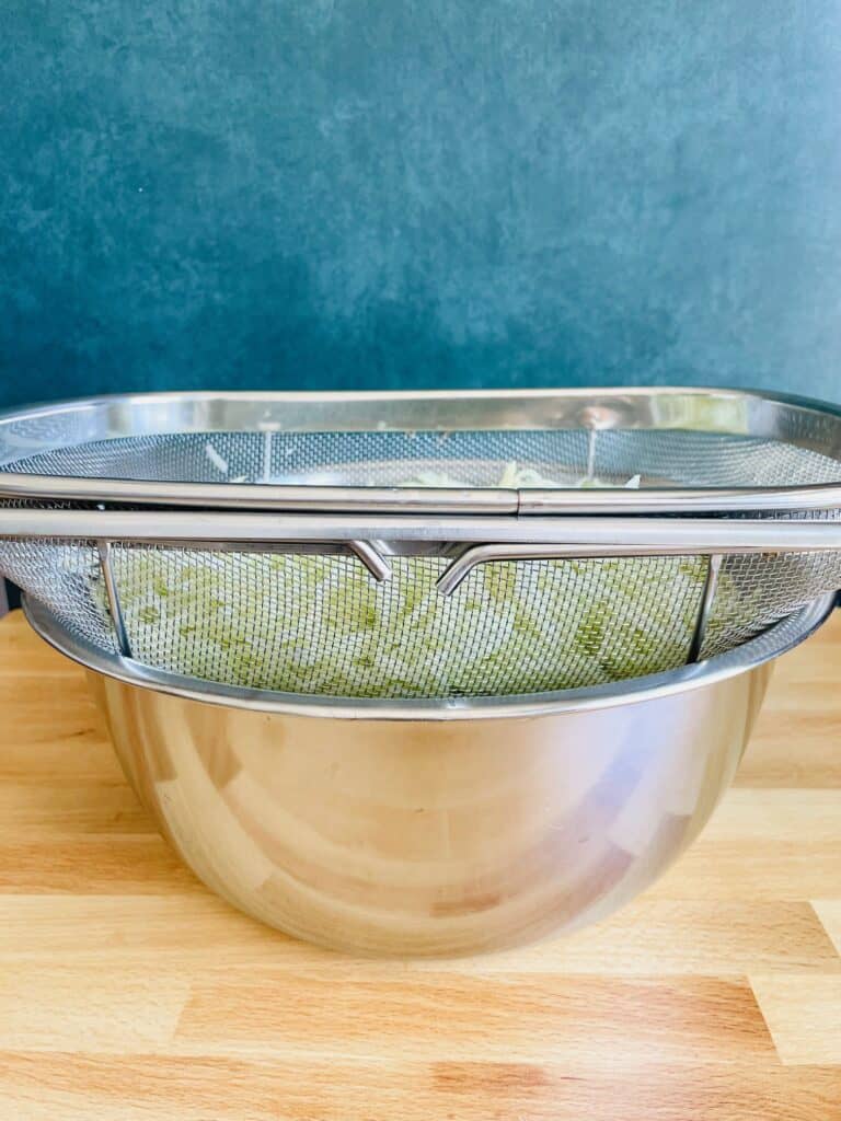 Shredded Chayote Squash Chouchou in colander over stainless steel bowl.